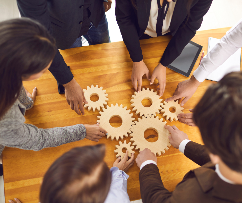 a group of people clustered around wooden gears on a table
